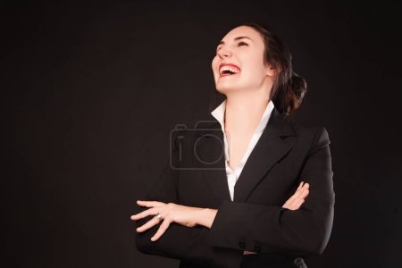 Junge Berufsfrau lacht herzlich im formellen schwarzen Anzug, ihr Ausdruck strahlt Freude und Zuversicht aus