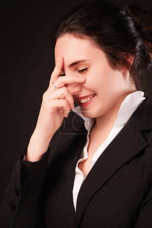 Professional young woman in a black business suit laughs while playfully hiding her face, showing a light-hearted spirit
