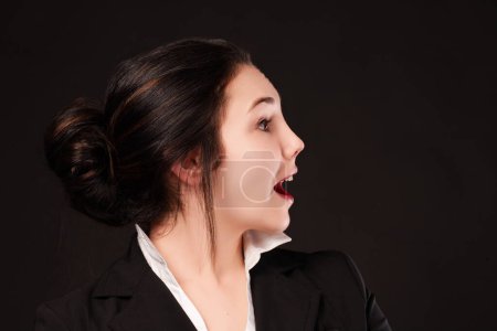 Expressive young professional shows a spontaneous reaction of surprise, her facial expression vivid against the dark backdrop