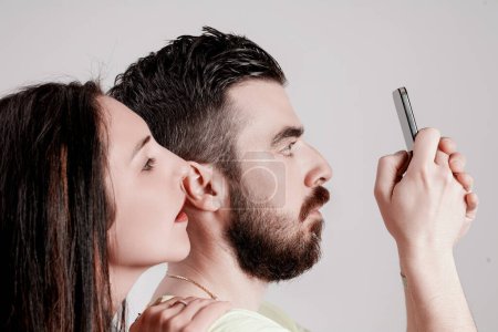 Mujer joven mira por encima del hombro de un hombre, mirando sigilosamente a la pantalla de su teléfono inteligente, un hábito común pero cuestionable moderno
