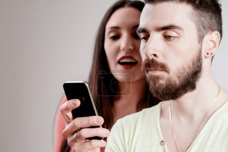 Er hält sein Telefon fest in der Hand, während sie eifrig seine Nachrichten liest und auf einen Vertrauensbruch hinweist.