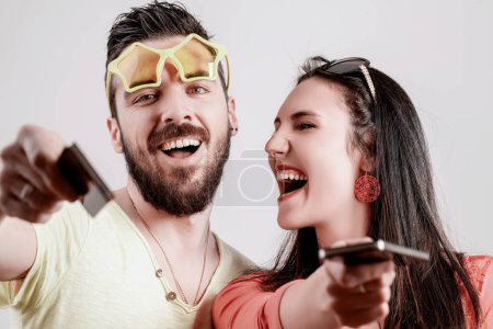 Couple laughs loudly, pointing their phones at the camera, their exuberance and loud demeanor drawing attention in a playful yet overwhelming way