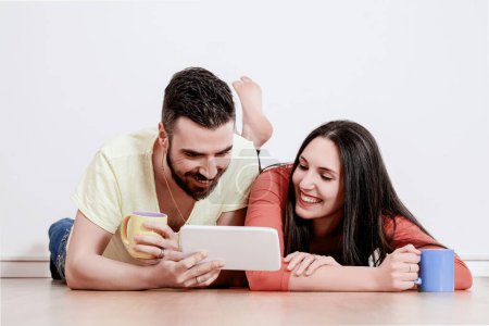 man and a woman lie comfortably on the floor, smiling as they watch something entertaining on a tablet