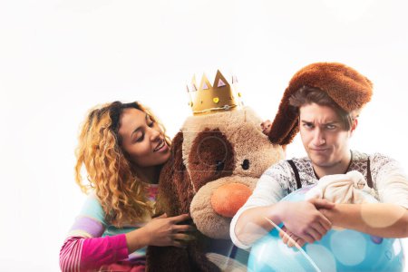 Candid photo of two people, possibly friends or siblings, in a playful moment with toys and a plush bear, smiling joyfully