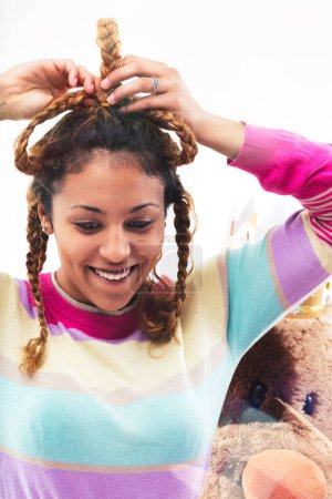 Smiling young woman with dreadlocks, wearing a vibrant sweater, seems to enjoy a festive atmosphere