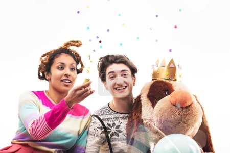 woman and a man in a playful setting, surrounded by balloons and a large teddy bear, engage in a light-hearted pretend play