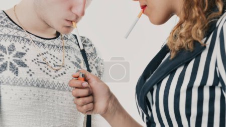 moment critique où un jeune homme et une jeune femme succombent à la pression de leurs pairs en fumant, soulignant les dangers de rechercher l'acceptation sociale