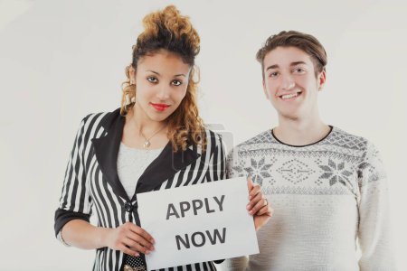 Jóvenes profesionales promueven una oportunidad, la mujer con un audaz cartel de 'Aplicar ahora', con un hombre de apoyo a su lado