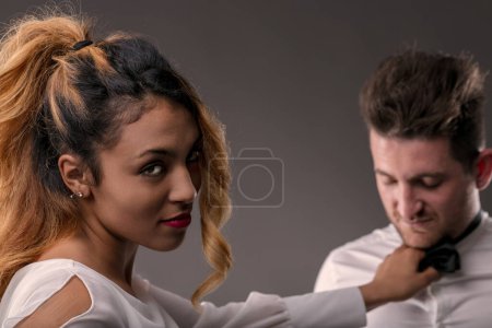 Powerful and sexy young woman adjusts the bow tie of a man who looks on with consent