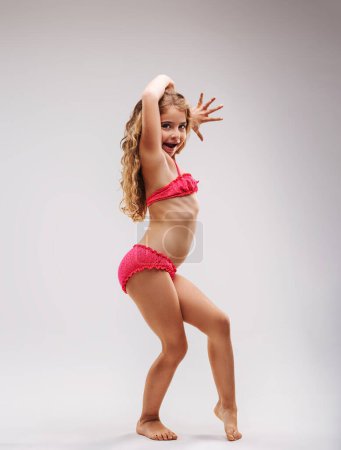 girl in a pink two-piece swimsuit flaunts her costume as if she were a celebrity model, posing with enthusiasm and conviction, eliciting contagious joy and sympathy