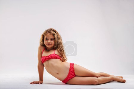 Brazenly confident little girl feels like a little mermaid as she stretches out to pose in her pink two-piece swimsuit. Far too confident!