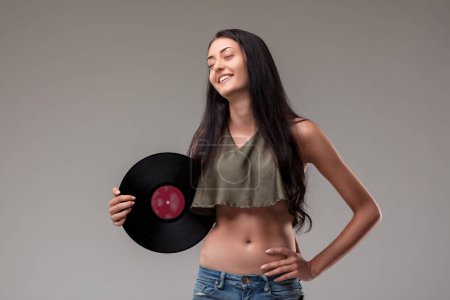 Joven mujer alegre en una camiseta corta sostiene un álbum de vinilo clásico, encarnando un estilo relajado