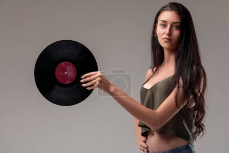 Poised young woman holding a vinyl, her serene face complemented by casual attire and a natural setting