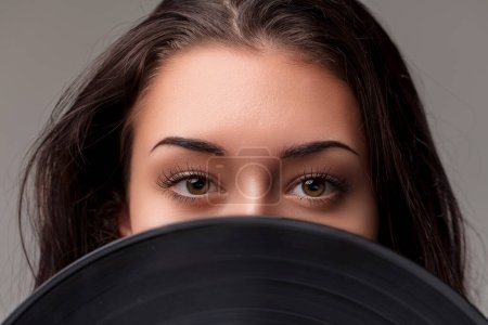 Close-up of captivating eyes looking over a vinyl record, blending playfulness with a musical theme