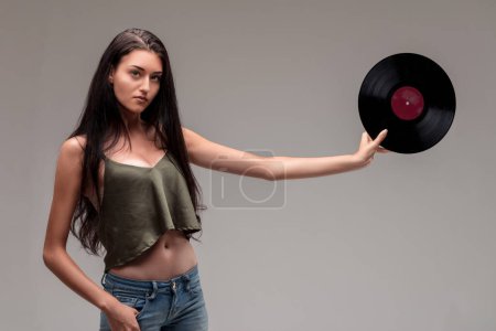 Confident young woman in a green tank top extends a vinyl record, her posture graceful and assured