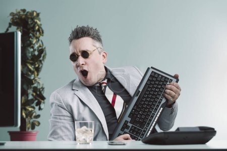 Geschäftsmann im hellgrauen Anzug imitiert mit seiner Computertastatur spielerisch einen Gitarristen voller Begeisterung
