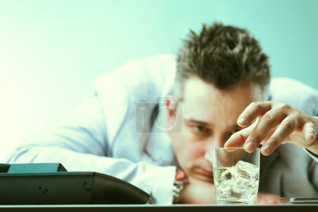 Abrumado por el estrés, un hombre recurre a beber en el trabajo, mostrando signos visibles de dependencia al alcohol