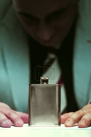 Man somberly contemplates a flask, symbolizing his struggle with alcohol addiction and its recognized health risks