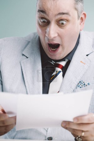Businessman looks shocked while reading a document, his exaggerated expression reflecting disbelief or unexpected news