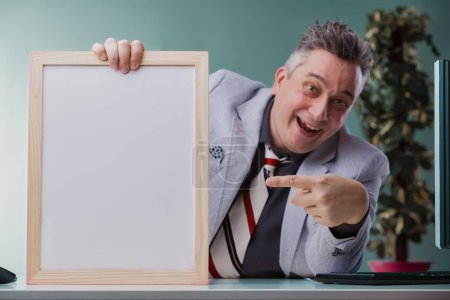 Fröhlicher Geschäftsmann im grauen Anzug zeigt verspielt auf ein leeres Whiteboard, bereit, frische Ideen zu präsentieren