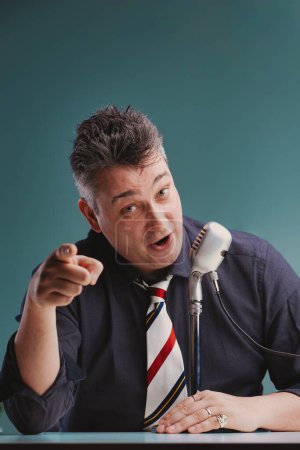 El carismático orador con camisa azul marino se dirige con confianza a su audiencia, señalando e interactuando directamente con ellos