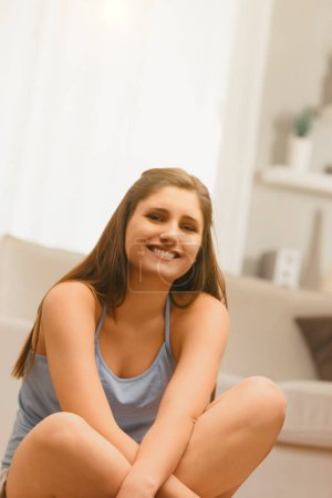 Smiling warmly, this young lady's relaxed posture in her living space adds a personal touch to her serene demeanor