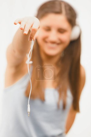 joyful young woman playfully holds out a headphone jack, her blurred smile indicating she's sharing her favorite music