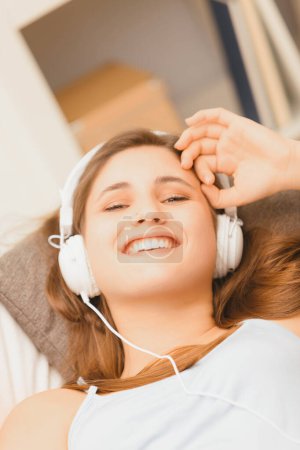 young woman lies back on her sofa, savoring the harmonious tunes from her headphones, embracing a calm moment