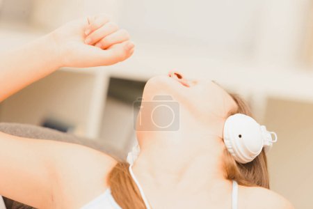Junge Frau singt fröhlich in ihrem Wohnzimmer, Kopfhörer auf und spürt den Rhythmus ihrer Lieblingsmusik