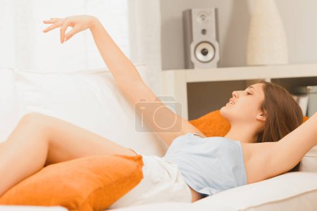 Mujer joven se estira lánguidamente en un sofá, sus brazos elegantemente levantados en un ambiente relajado en casa