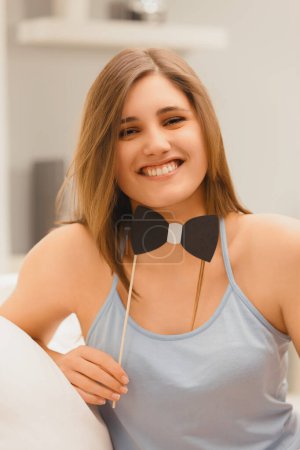 With a genuine smile, a young woman playfully presents a black bow tie, enhancing her spirited expression