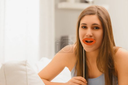 Engaging and humorous, a woman uses a paper red lips prop, adding a playful touch to her expression