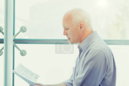 Thoughtful senior examines crucial end-of-life planning papers, considering his future health and retirement strategies in a serene setting