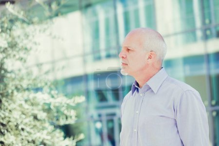 Man with light beard stands outdoors near modern architecture, exuding a calm and assured professional presence in a blue shirt