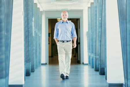 Elderly man with a confident walk, dressed in a blue shirt and light pants, strolls in a well-lit hallway