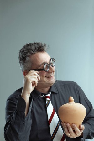 Wearing a dark shirt and striped tie, the man sports comical glasses and holds a clay pot. His playful smile and quirky look contribute to a humorous and lighthearted atmosphere
