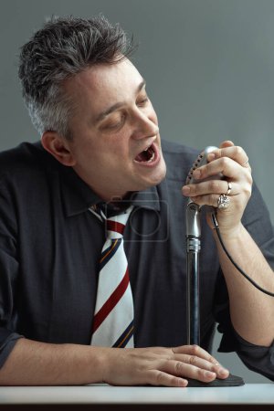 hombre de mediana edad con una camisa oscura y corbata a rayas ofrece un discurso ferviente en un micrófono vintage. Su intensa expresión y fuerte agarre indican que está difundiendo propaganda.