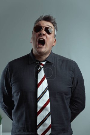 middle-aged man wearing sunglasses and a striped tie yells, possibly giving orders. His dark shirt and open mouth convey intense emotion, suggesting authority and urgency in a tense situation