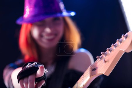Junge Frau mit kastanienbraunem Haar, glitzerndem Hut und dunklem Glitzertop spielt lächelnd eine E-Gitarre. Ihr selbstbewusster und fröhlicher Auftritt auf der Bühne zeigt ihr musikalisches Talent