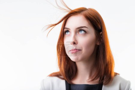playful-looking woman with auburn hair in a professional outfit gazes upward, her hair lifted by her blowing. Her expression and messy hair bring a whimsical touch to her appearance