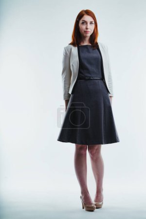 Sophisticated young woman in a dark dress and light gray blazer stands poised, her gaze steady and confident