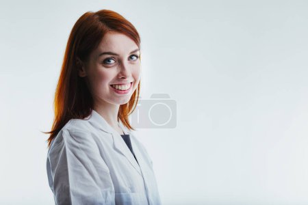 une femme aux cheveux roux souriante en blouse de laboratoire souligne son rôle en tant qu'experte et chercheuse chevronnée en technologie, plusieurs doctorats soulignant son excellence académique et professionnelle