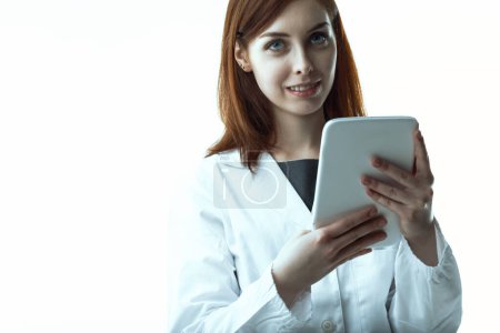 mujer sonriente con pelo castaño, vestida con una bata blanca de laboratorio, sostiene una tableta. Su comportamiento confiado y accesible refleja competencia y profesionalidad en un entorno médico