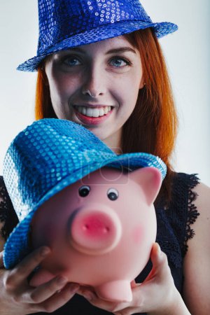 oung woman with red hair, wearing a black lace top, smiles brightly while holding a pink piggy bank close to her face, her joyful expression reflecting financial optimism and savings