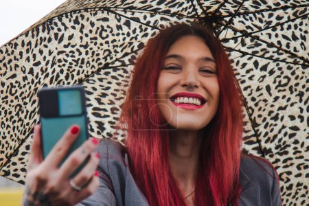 Téléchargez les photos : Influenceuse fille avec parapluie et téléphone portable sous la pluie prendre un selfie - en image libre de droit