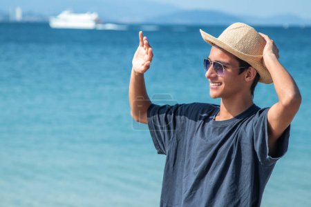 Téléchargez les photos : Jeune homme avec chapeau sur la plage agitant la main - en image libre de droit