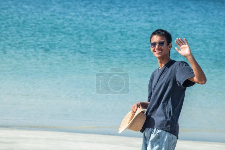 Téléchargez les photos : Jeune latin hispanique homme avec chapeau sur la plage agitant la main - en image libre de droit