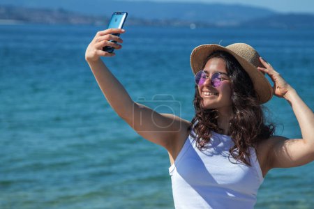 Téléchargez les photos : Fille prendre un selfie ou vidéo en direct sur la plage - en image libre de droit