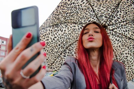 Téléchargez les photos : Fille avec parapluie sous la pluie envoyer un baiser par téléphone mobile - en image libre de droit