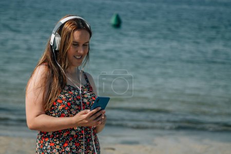 Téléchargez les photos : Femme courbée sur la plage avec téléphone et écouteurs - en image libre de droit